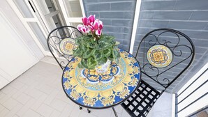 A round table with a decorative blue and yellow pattern, a potted plant with pink flowers, and black metal chairs. - MARINELLI HOUSE - Song'Parthenope - Naples (Napoli)