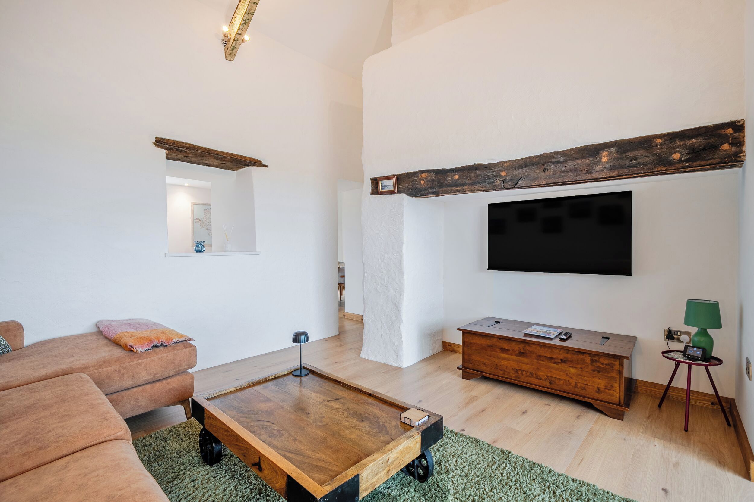 Uma sala de estar moderna com uma mesa de centro de madeira, um sofá, uma TV fixada na parede e uma pequena mesa lateral com abajur.