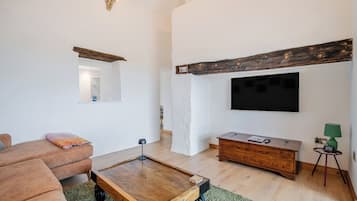 Uma sala de estar moderna com uma mesa de centro de madeira, um sofá, uma TV fixada na parede e uma pequena mesa lateral com abajur.