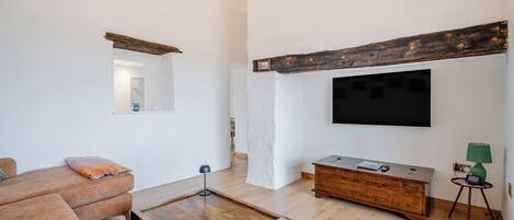 A modern living room with a wooden coffee table, a sofa, a TV mounted on the wall, and a small side table with a lamp.