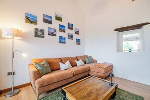 A living room with a sectional sofa, a coffee table, a floor lamp, and a wall adorned with landscape photographs. - Hen Penmynydd (Holyhead)