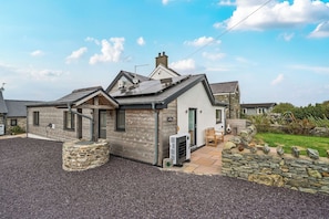 A two-story house with a stone foundation, a grey wooden exterior, and a tiled roof. - Hen Penmynydd (Holyhead)