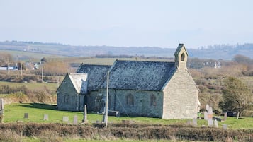A stone church with a steeply pitched roof and a bell tower, surrounded by a cemetery with headstones.