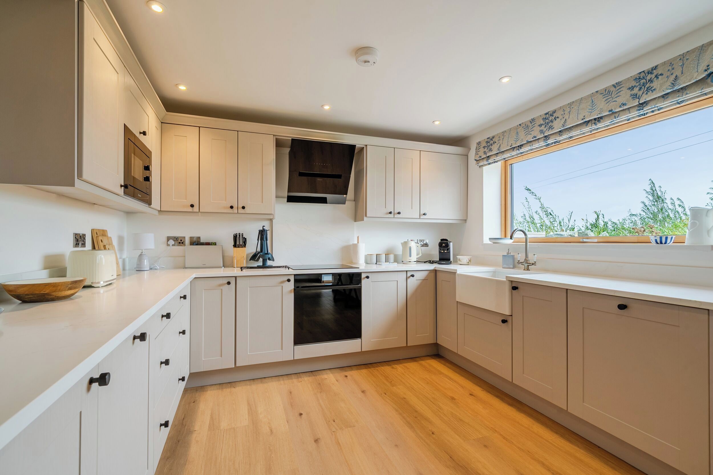 Una cocina moderna con armarios blancos, horno empotrado y ventana con vistas a zonas verdes.