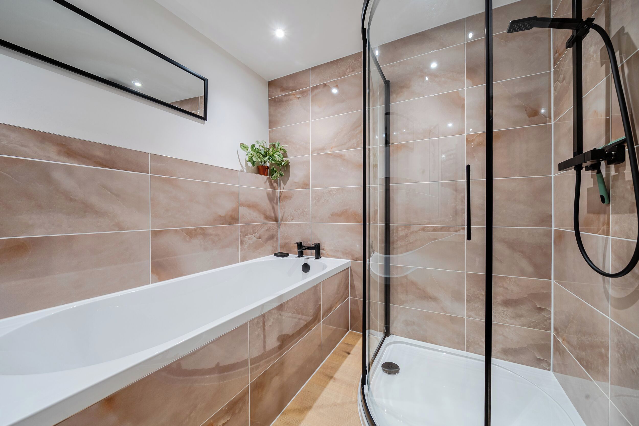 Un baño moderno con ducha envuelta en vidrio, una bañera blanca y una planta en maceta en la pared.