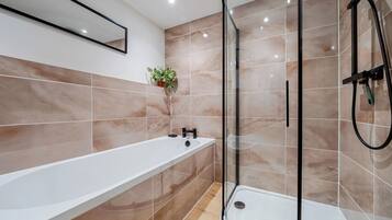 Un baño moderno con ducha envuelta en vidrio, una bañera blanca y una planta en maceta en la pared.