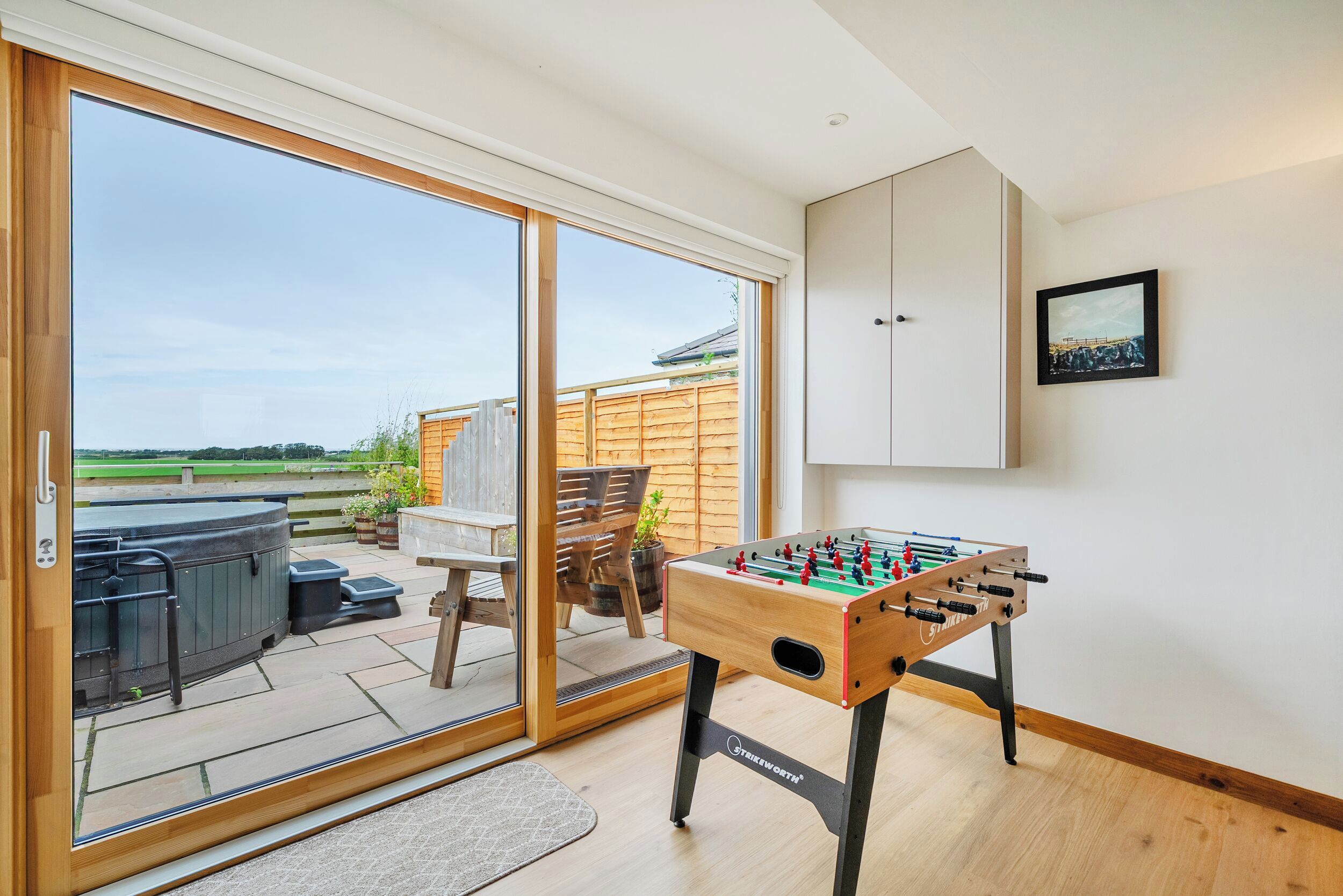 Een kamer met een tafelvoetbaltafel, een schuifdeur naar een buitenruimte en een houten terras.
