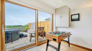 Een kamer met een tafelvoetbaltafel, een schuifdeur naar een buitenruimte en een houten terras.