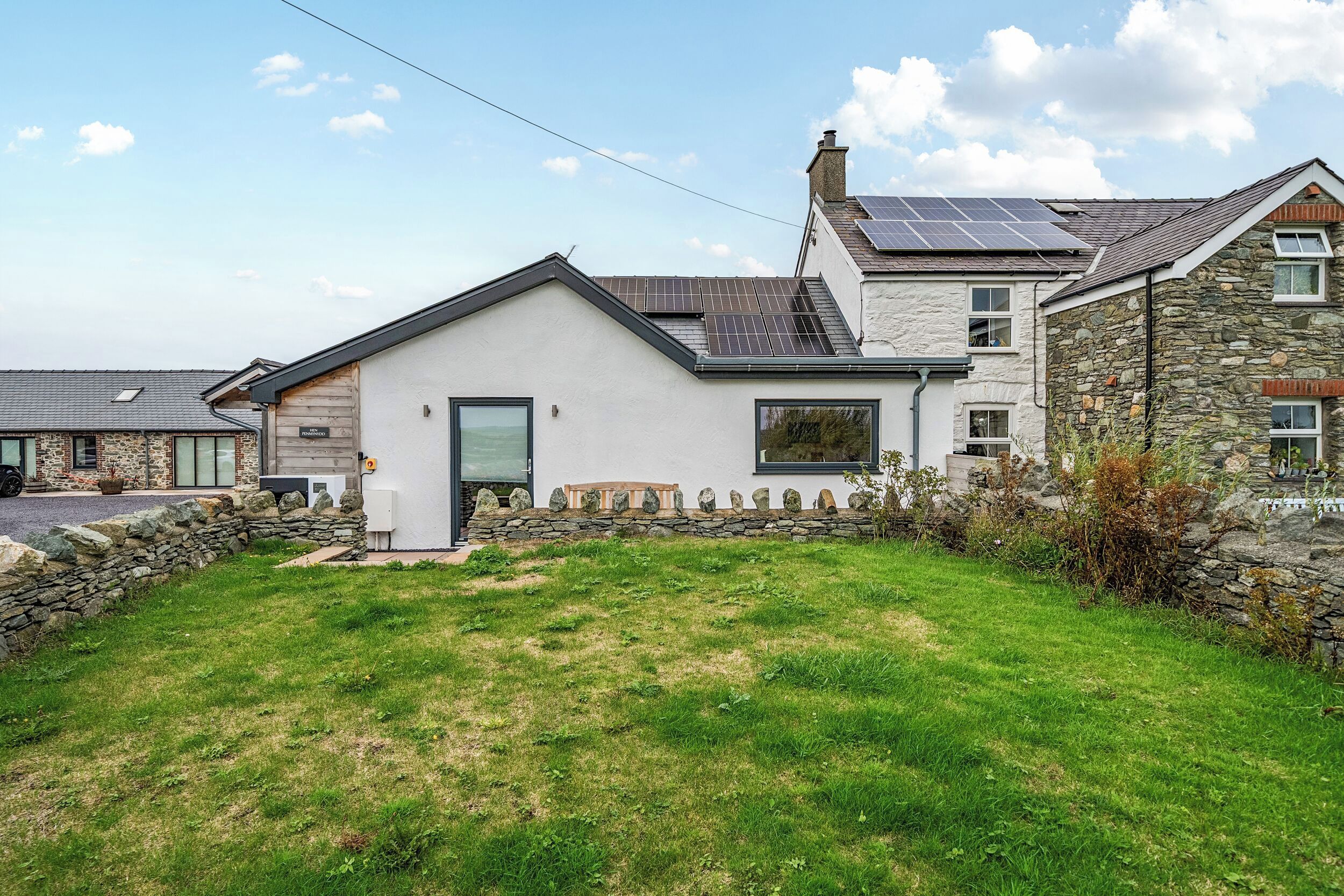 A two-story house with a stone facade, a sloped roof, and solar panels.