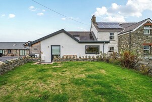 Una casa de dos pisos con fachada de piedra, techo inclinado y paneles solares.