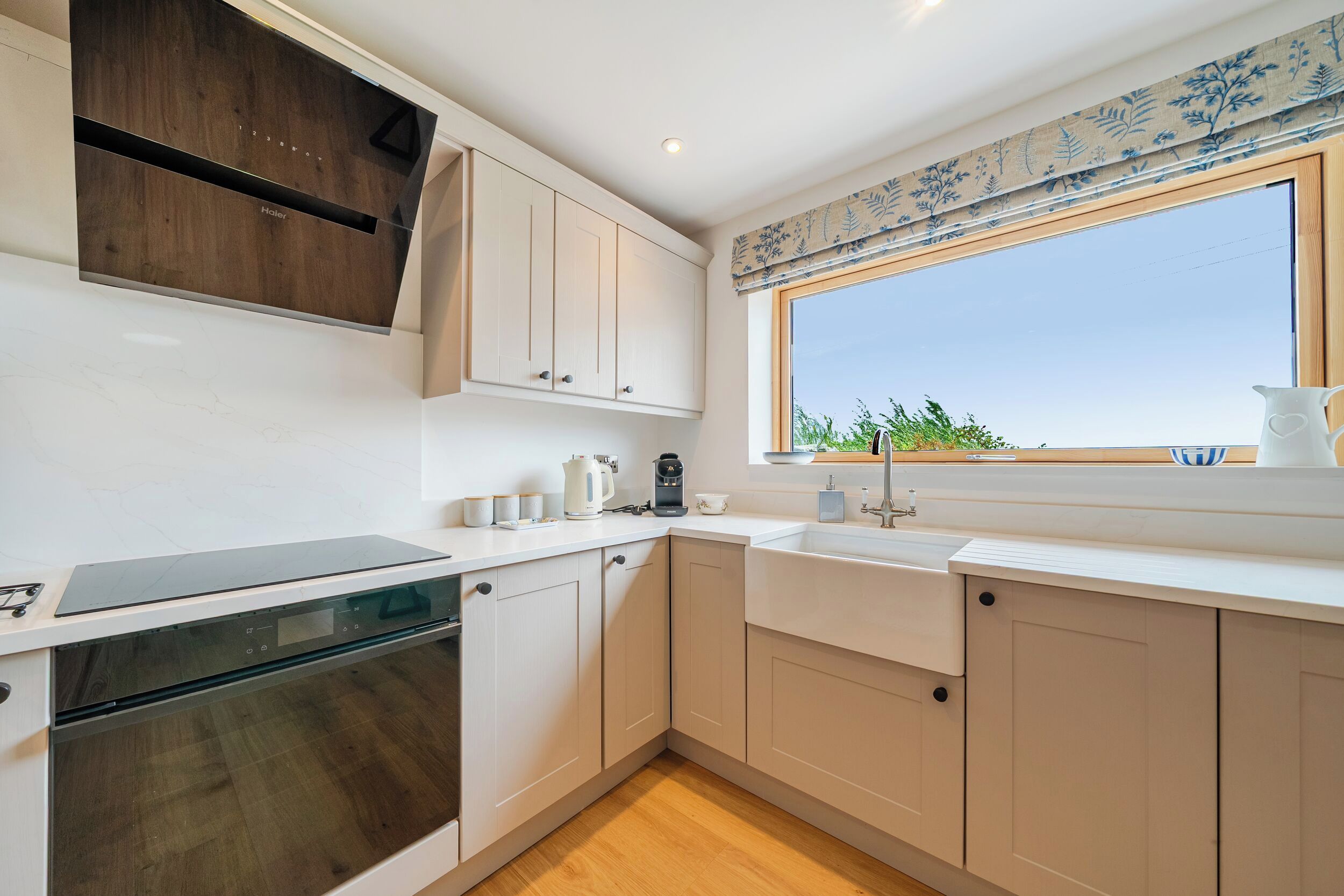Eine moderne Küche mit weißen Schränken, einem eingebauten Ofen, einem großen Fenster mit Aussicht und einer Holz Arbeitsplatte.