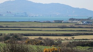 A coastal landscape with a bridge, fields, and distant mountains.