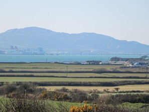 Un paysage côtier avec un pont, des champs et des montagnes à l’horizon.