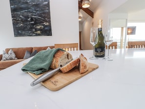 A dining area with a wooden cutting board, a knife, a loaf of bread, and a bottle of wine on a table. - 2 Trem Y Mor (Holyhead)
