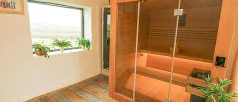 A sauna room with a wooden sliding door, a window with plants, and a tiled floor.