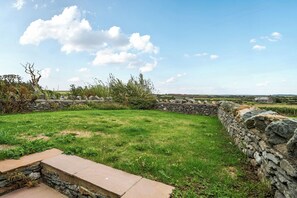 Un mur de pierre, une zone herbeuse et un ciel dégagé.