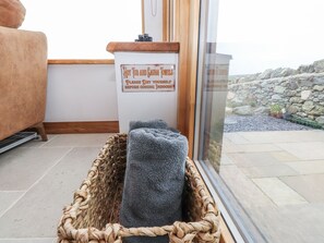 A spa area with a sign indicating hot tub and sauna towels, a woven basket with towels, and a stone wall outside. - 2 Trem Y Mor (Holyhead)