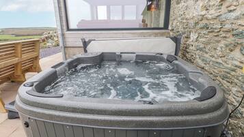 A hot tub with a stone exterior, a wooden bench, and a stone wall.