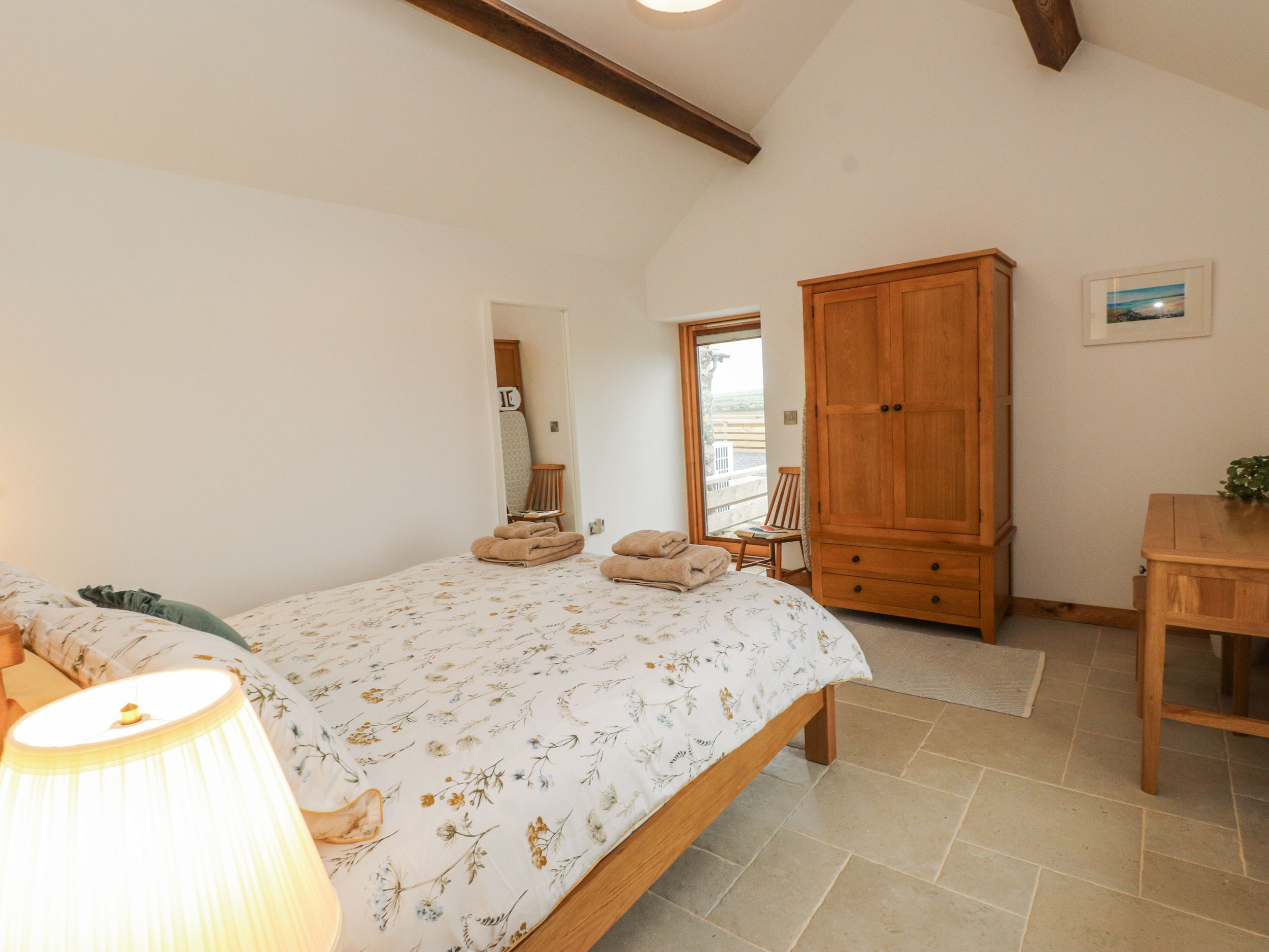 A bedroom with a bed, a wooden wardrobe, a chair, and a table.