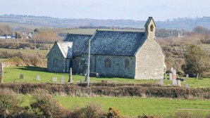 A stone church with a steeply pitched roof and a bell tower, surrounded by a cemetery with headstones.