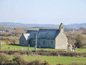 Une église en pierre, dotée d’un toit à forte pente et d’un clocher, entourée d’un cimetière où se dressent des pierres tombales.