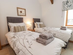 A twin bedroom with two beds, each with floral bedding and a headboard. There is a bedside table with a lamp and a framed picture on the wall. - 2 Trem Y Mor (Holyhead)