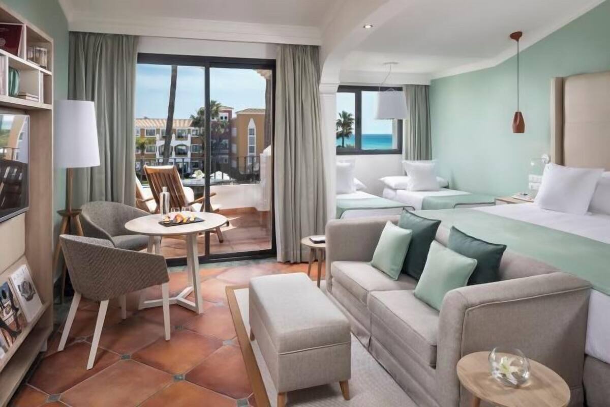Ein Hotelzimmer mit Balkon, einer Couch, einem Esstisch und einem Bett.