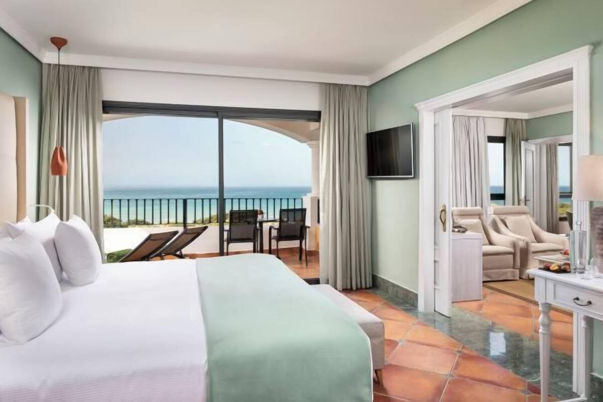 Ein Hotelzimmer mit Bett, Fernseher, Balkon und Meerblick sowie einem Sessel.