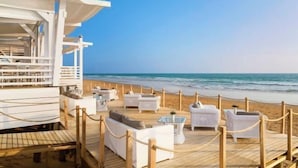 Eine Strandlounge mit weißen Korbmöbeln und einem Holzdeck mit Blick auf den Ozean.