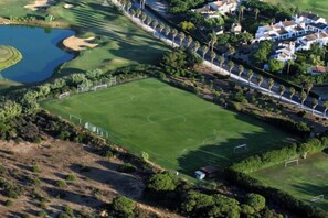 An aerial view of a golf course with a pond, surrounded by residential buildings and trees.