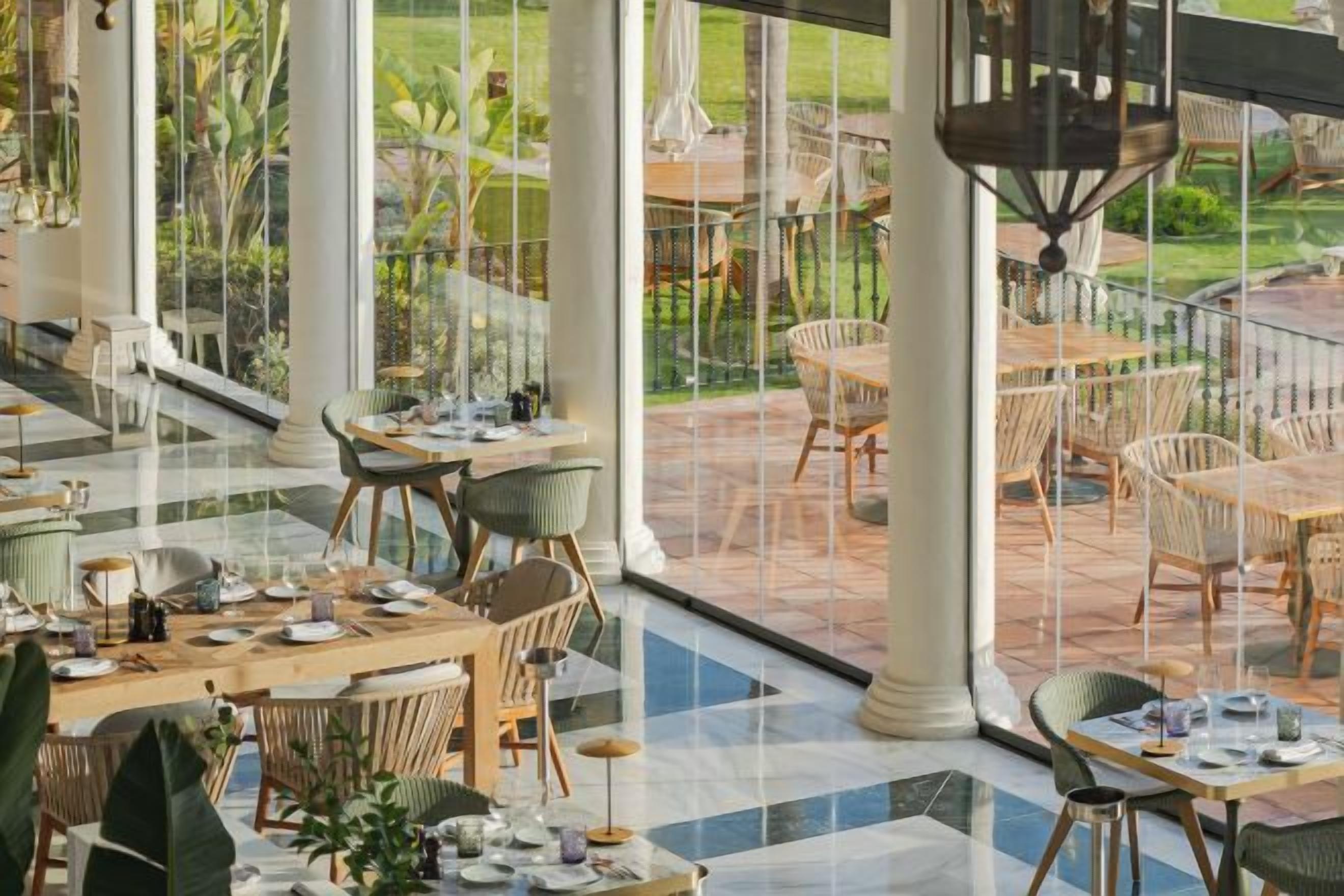 An indoor dining area with tables and chairs, large windows, and a view of the outdoor patio.