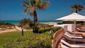 Ein Strandresort mit Liegestühlen und Sonnenschirmen, ein Weg zum Strand und Palmen.