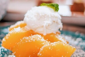 A dessert with a scoop of ice cream on top of fruit, possibly peach or mango, with a garnish of green leaves. - Palacio de Sancti Petri Gran Melia (Novo Sancti Petri)