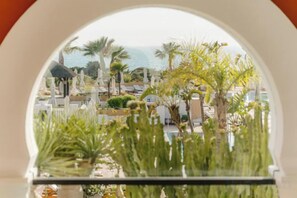 A view through an arched window of a resort with outdoor seating and palm trees. - Palacio de Sancti Petri Gran Melia (Novo Sancti Petri)