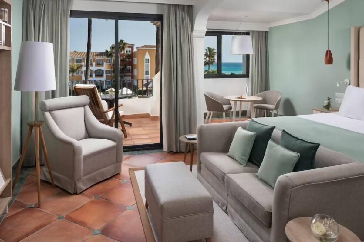Ein Hotelzimmer mit Balkon, einer Couch, einem Sessel, einem kleinen Tisch und einem Bett.