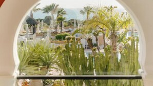 Blick durch ein rundes Fenster auf ein Resort mit Palmen, Liegestühlen und einem Pool.