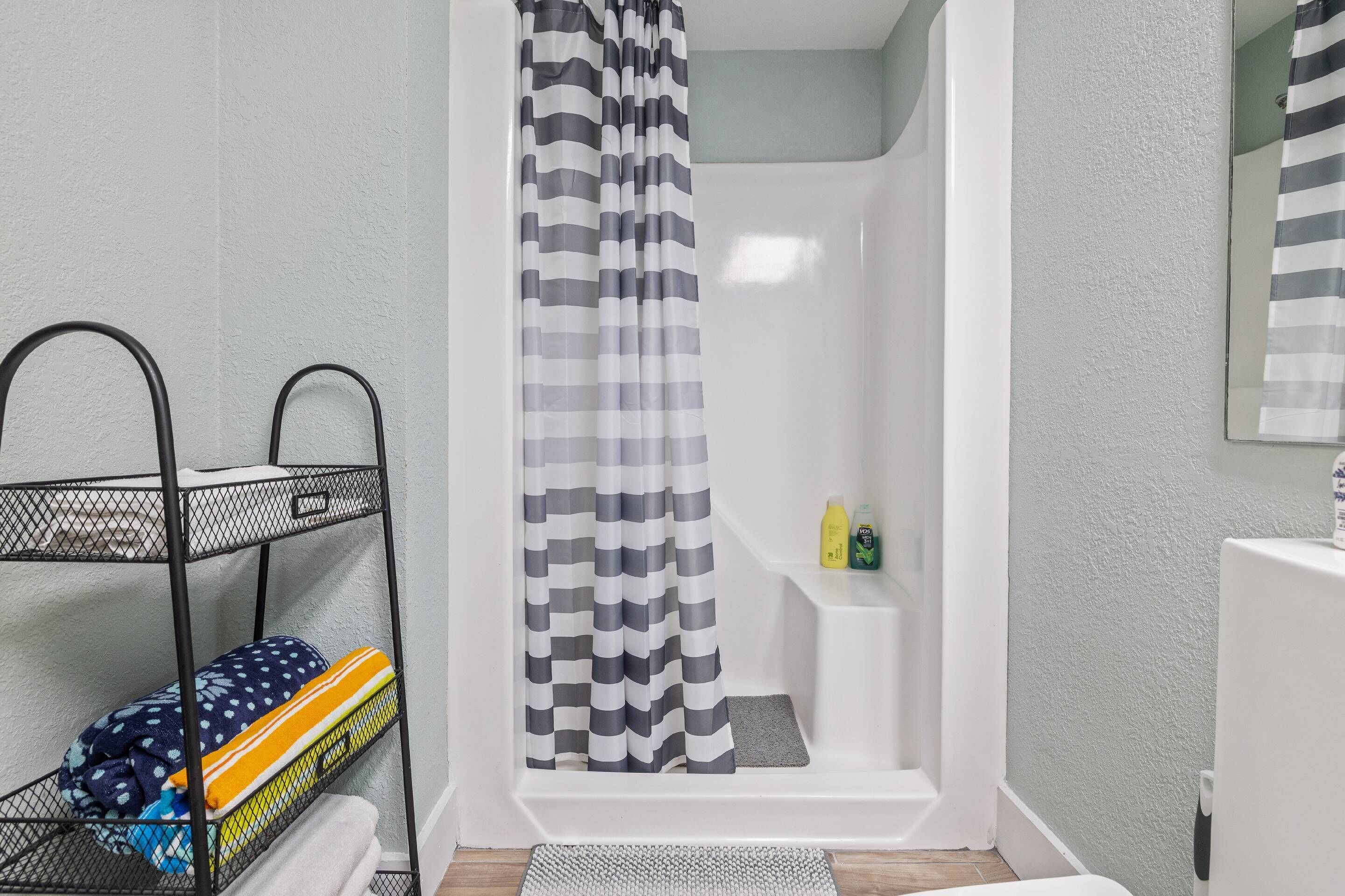 A bathroom with a shower, a metal shelf with towels, and toiletries on a shelf.