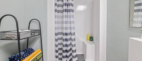 A bathroom with a shower, a metal shelf with towels, and toiletries on a shelf.