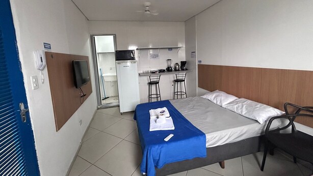 A compact hotel room with a bed, a small desk with a chair, a microwave, and a coffee maker.