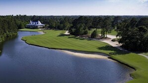 A golf course with a clubhouse, surrounded by trees and a body of water.