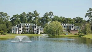 A residential area with two-story houses, a pond with fountains, and a well-maintained lawn.