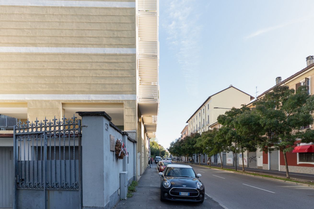 A street with a black car parked on the side, buildings on both sides, and a clear sky.