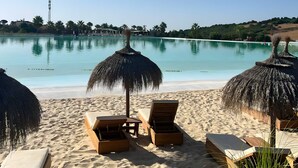 Une plage avec des chaises longues et des parasols en chaume, un ciel bleu dégagé et une mer calme.