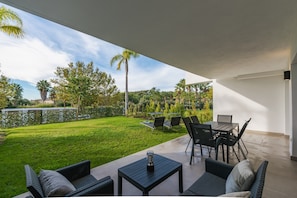 An outdoor patio with a table and chairs, a grassy lawn, and a view of trees and a body of water.