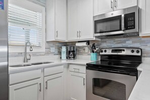 Una cocina moderna con armarios blancos, un refrigerador de acero inoxidable, una estufa negra y un microondas.