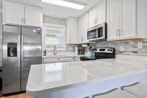 Une cuisine moderne dotée d’appareils électroménagers en acier inoxydable, de meubles blancs et d’un grand îlot central.