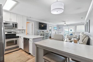 Une cuisine moderne dotée d’appareils électroménagers intégrés, un coin repas avec un grand îlot central et un salon avec un canapé et un téléviseur.