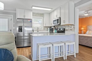 Une cuisine moderne avec des meubles blancs, un réfrigérateur en acier inoxydable, un four à micro-ondes et une cuisinière. On y trouve également un coin bar avec des tabourets et une fenêtre équipée de stores.