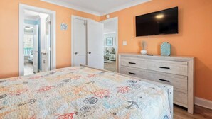 Un dormitorio con cama, cómoda, televisor y puerta que da a otra habitación.