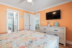 Une chambre à coucher comprenant un lit, une commode, un téléviseur et une porte donnant sur une autre pièce.